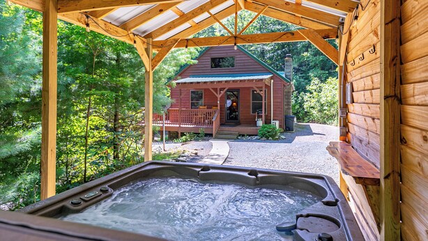 Una cabaña de madera con un jacuzzi en primer plano, rodeada de abundante vegetación.