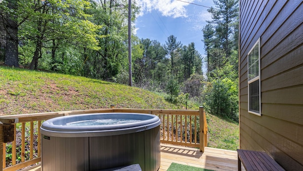 Un bain à remous sur une terrasse en bois, avec vue sur une colline boisée.