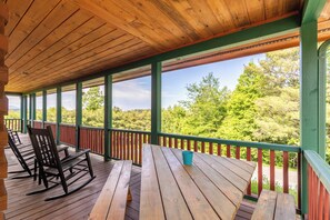 A covered wooden deck with benches and a picnic table, overlooking a forested area. - Good Medicine (Boone)
