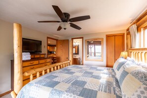 Un dormitorio con cama, televisor, ventilador de techo, muebles de madera y una ventana.