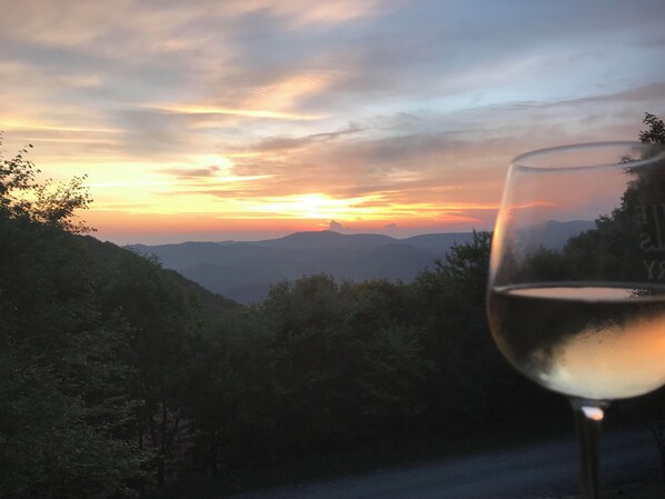 Een glas witte wijn met uitzicht op een bergachtig landschap bij zonsondergang.