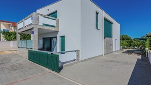 A modern two-story building with a flat roof, a balcony on the upper floor, and a garage door on the ground floor. - Apartment Marovic (Vir)