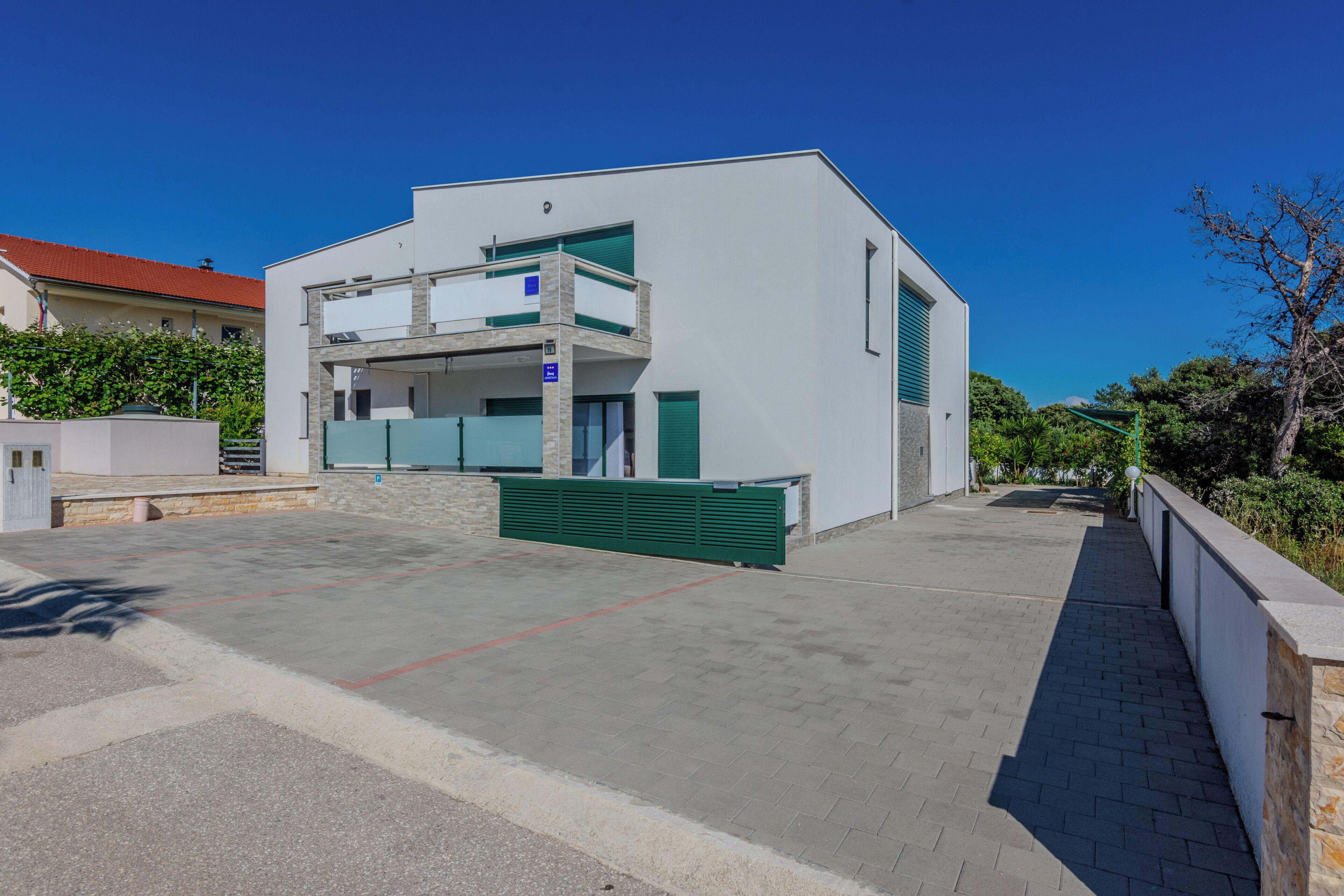 Un edificio moderno a due piani con tetto piatto, un balcone e un vialetto lastricato.
