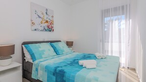 A bedroom with a bed, two bedside tables, a wall-mounted artwork, and a window with sheer curtains. - Apartment Marovic (Vir)