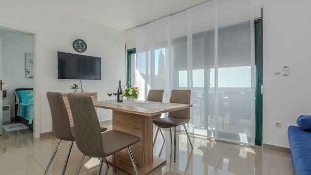 A modern living room with a dining table, chairs, a flat-screen TV, and a large window. - Apartment Marovic (Vir)