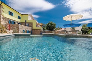 A pool area with clear blue water, lounge chairs, and umbrellas. - Villa Melary with the Pool, Jacuzzi & Ps5 surrounded with nature. (Kras)