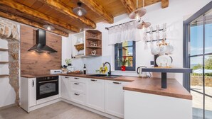 A modern kitchen with white cabinets, a built-in oven, wooden countertops, and a stone wall. - Villa Melary with the Pool, Jacuzzi & Ps5 surrounded with nature. (Kras)
