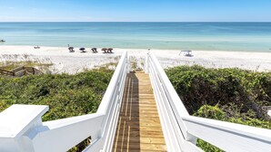 A wooden boardwalk leading to a beach with white sand and clear blue water.
