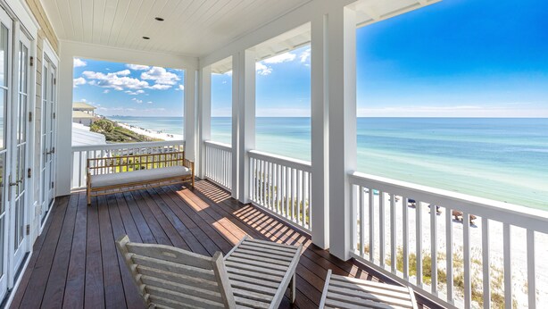 A covered porch with a wooden floor, white railings, and a bench.