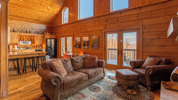 A log cabin interior with a kitchen, dining area, and living room furnished with leather sofas and a patterned rug. - Faraway Skies (Zionville)