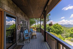 A wooden deck with outdoor seating, a view of mountains, and a hanging flower basket. - Chipmunk View Lodge (Blowing Rock)