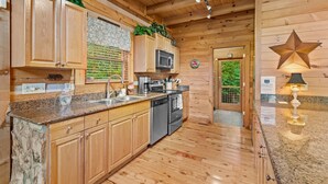 A wooden cabin-style kitchen with granite countertops, wooden cabinets, a microwave, a sink, and a stove. - Pretty Spectacular (Banner Elk)
