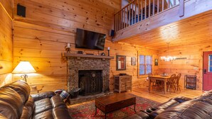 A cozy log cabin interior with a fireplace, leather sofas, a dining area, and a TV mounted on the wall. - Cozy Cabin (Vilas)