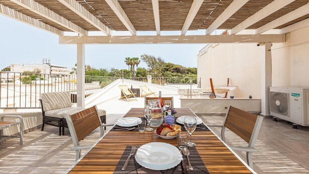 An outdoor dining area with a wooden table set for two, surrounded by wicker chairs, a fan, and a water dispenser. - 4002 Villetta Playa del Sol by Barbarhouse (Manduria)