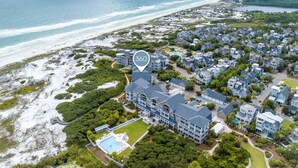 An aerial view of a coastal residential area with a large house featuring a swimming pool, surrounded by smaller houses and a beach. - Dune Trails | Beach Access | Shared Pool (Watersound)