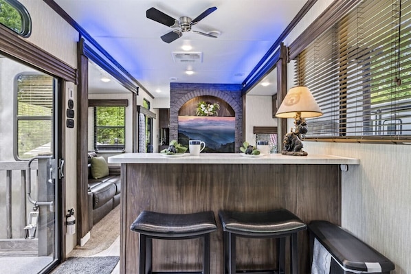 A kitchen area with a bar counter, seating, and a ceiling fan.