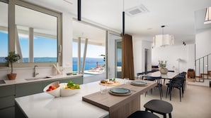 Une cuisine moderne dotée d’un grand îlot central, d’un coin repas avec une longue table et d’une vue sur la mer.
