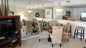 A modern living room with a dining area, a kitchen, and a large mirror reflecting the space. - Pelican Beach 1508 1 Bedroom Home (Destin)
