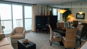A living room with a sofa, chairs, a dining table, and a TV stand. - Pelican Beach 1508 1 Bedroom Home (Destin)