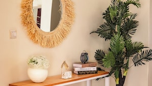 A wooden console table with a woven mirror, a potted plant, and decorative items. - Akiiro Homes (Kampala)