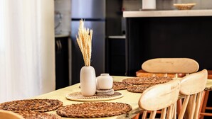 A dining area with a wooden table, woven placemats, and wooden chairs. There is a vase with dried plants on the table. - Akiiro Homes (Kampala)