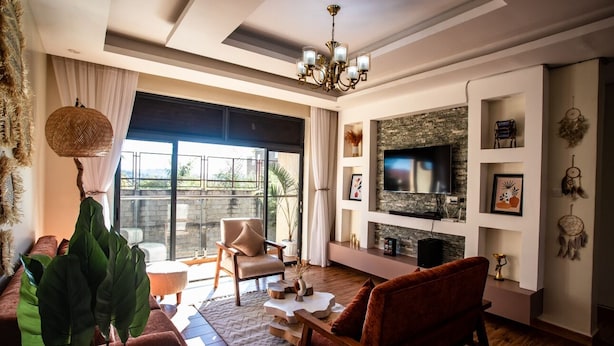 A modern living room with a large TV, comfortable seating, and a view to the outdoors. - Akiiro Homes (Kampala)
