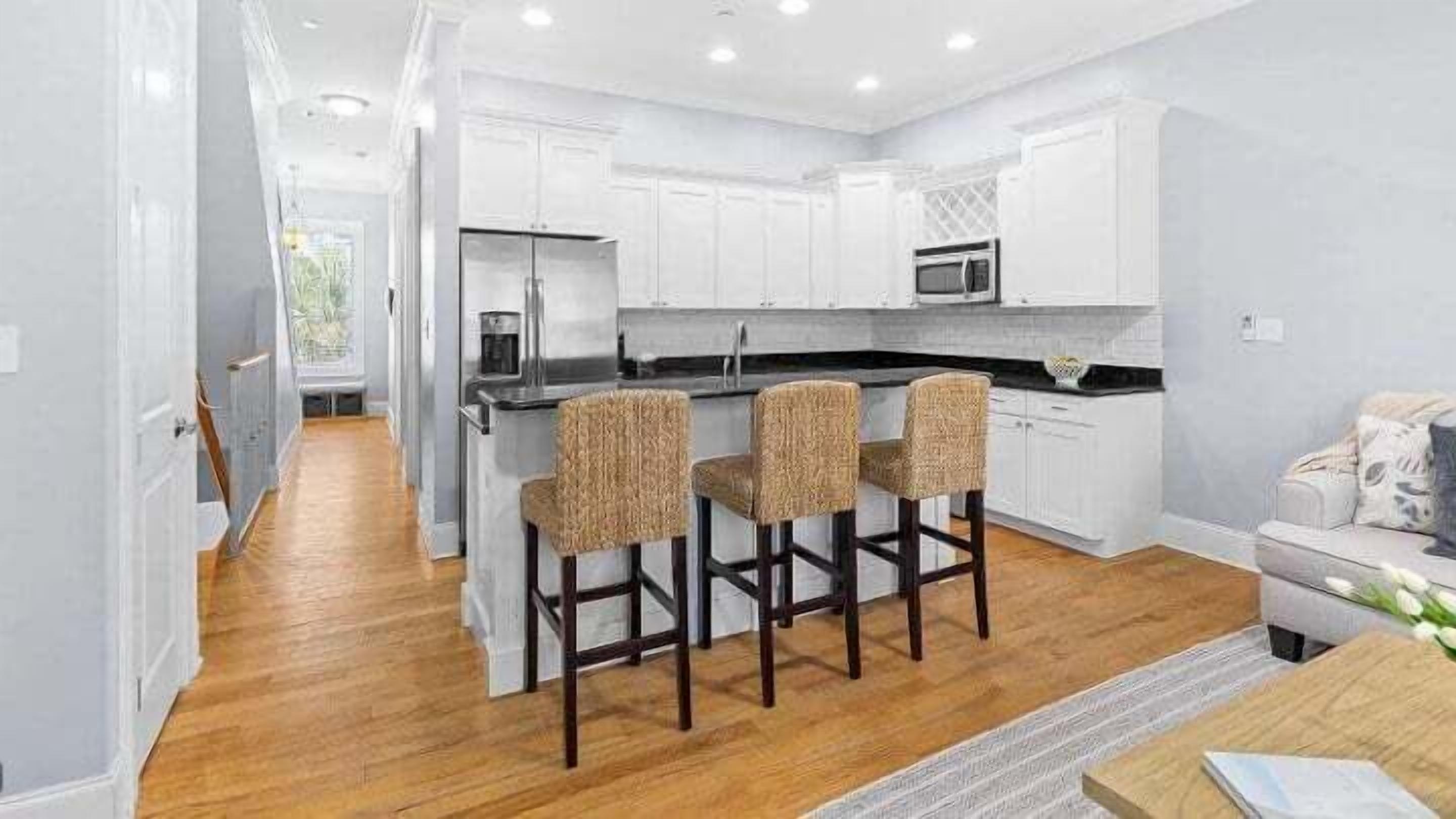 A modern kitchen with white cabinetry, a central island with bar stools, and a microwave above the island.