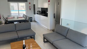 A modern apartment with grey sofas, a wooden coffee table with a bottle and glasses, a kitchen area, and a dining table with chairs. - Casa Isa, Idéalement Située Dans la Vielle Ville, Offre une Incroyable vue mer (Albufeira)