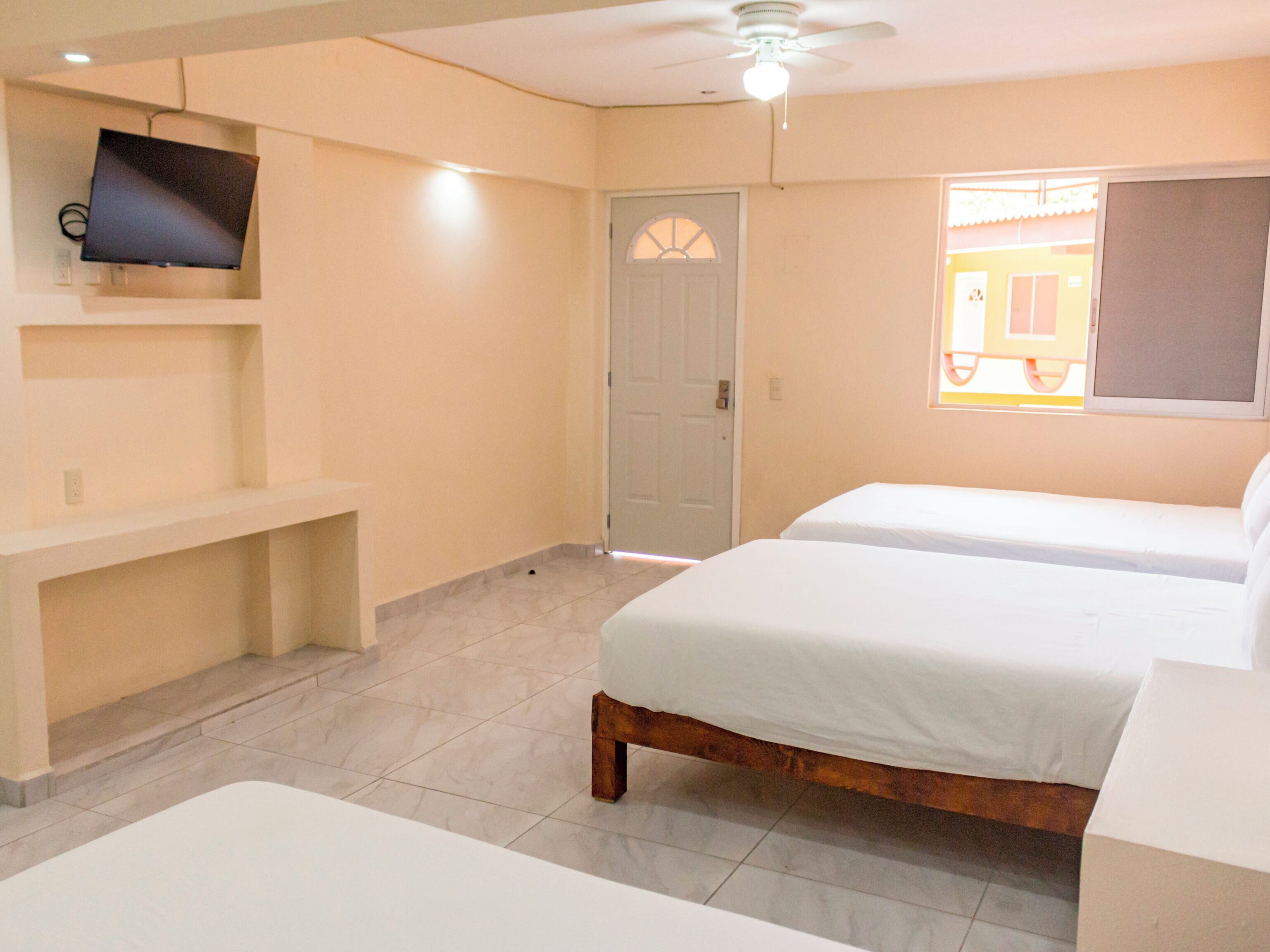 A hotel room with two beds, a TV on the wall, a ceiling fan, and a door.