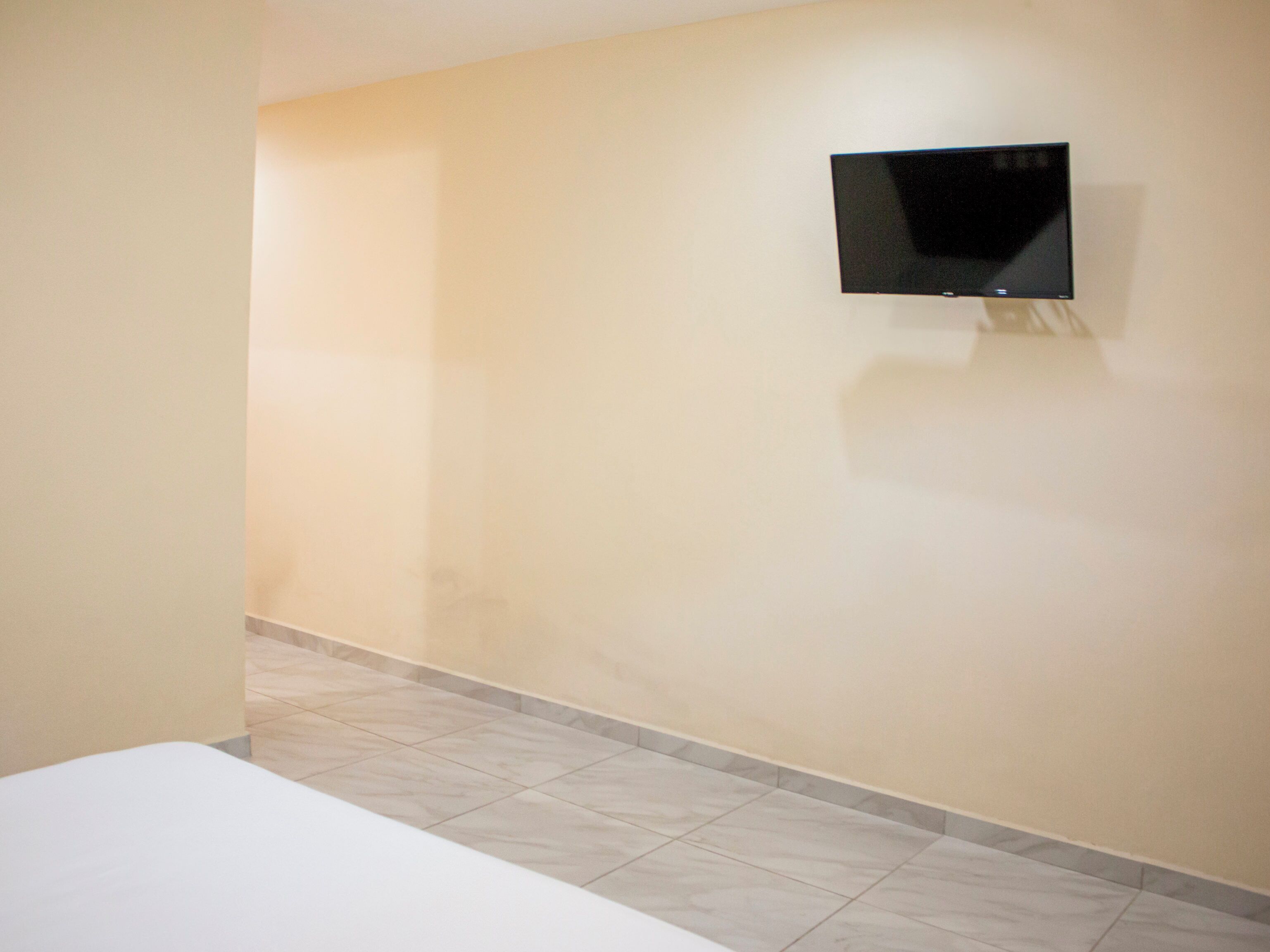 Quarto de hotel com cama, TV de tela plana na parede e piso cerâmico.