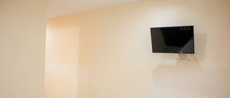A hotel room with a bed, a flat-screen TV mounted on the wall, and a tiled floor.