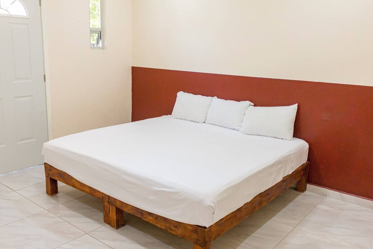 A single bed with a wooden frame and white bedding in a room with white tiled flooring and a red accent wall.