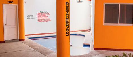 A pool area with a sign listing pool rules in Spanish, a white door, and orange walls.