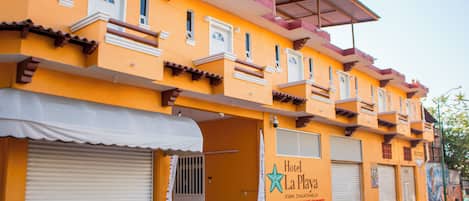 Un hôtel à la façade jaune, doté de nombreux balcons et dont les volets sont fermés.