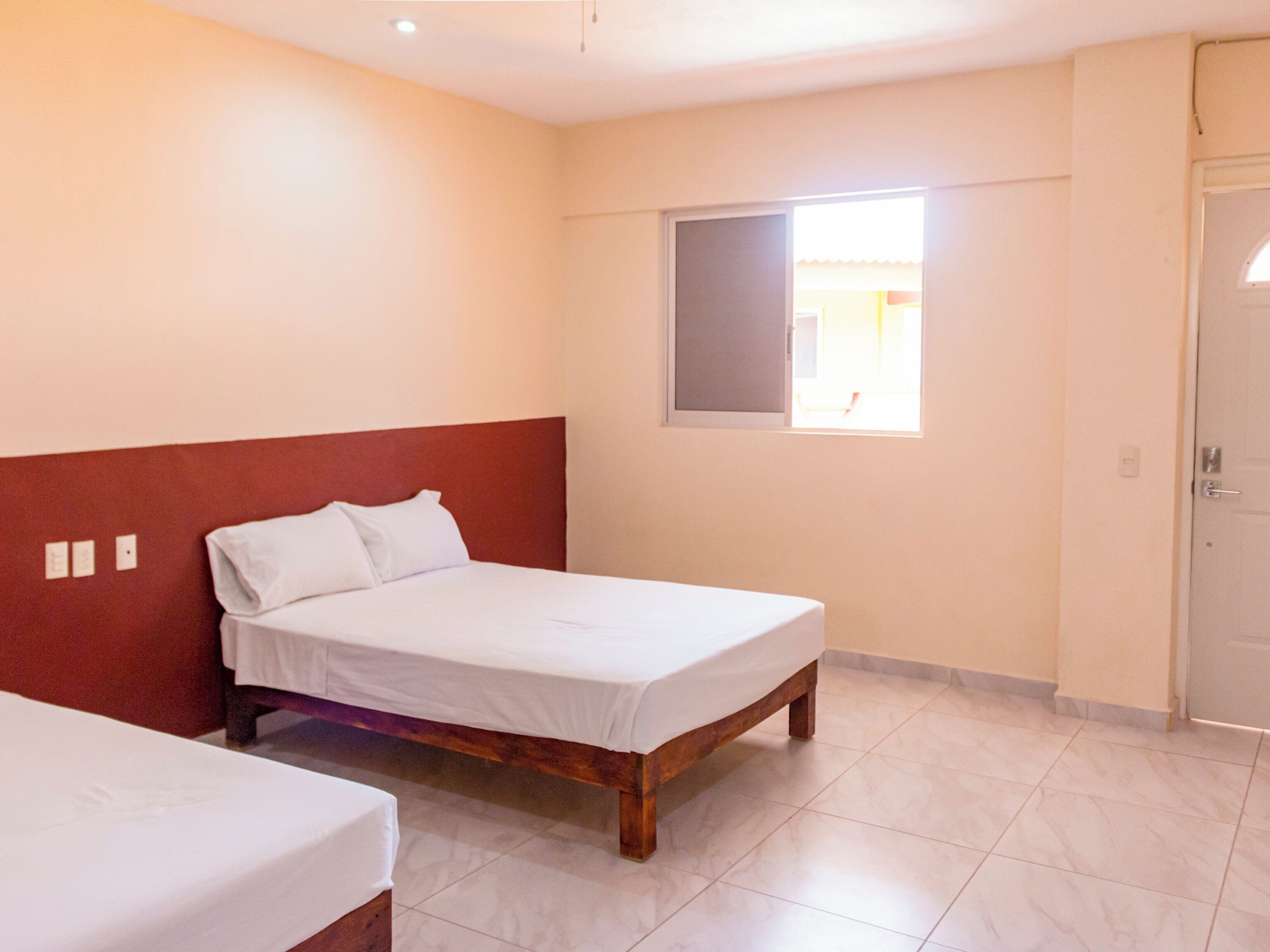 Una habitación con una cama individual, cabecera de madera, ventana con vistas y una puerta.