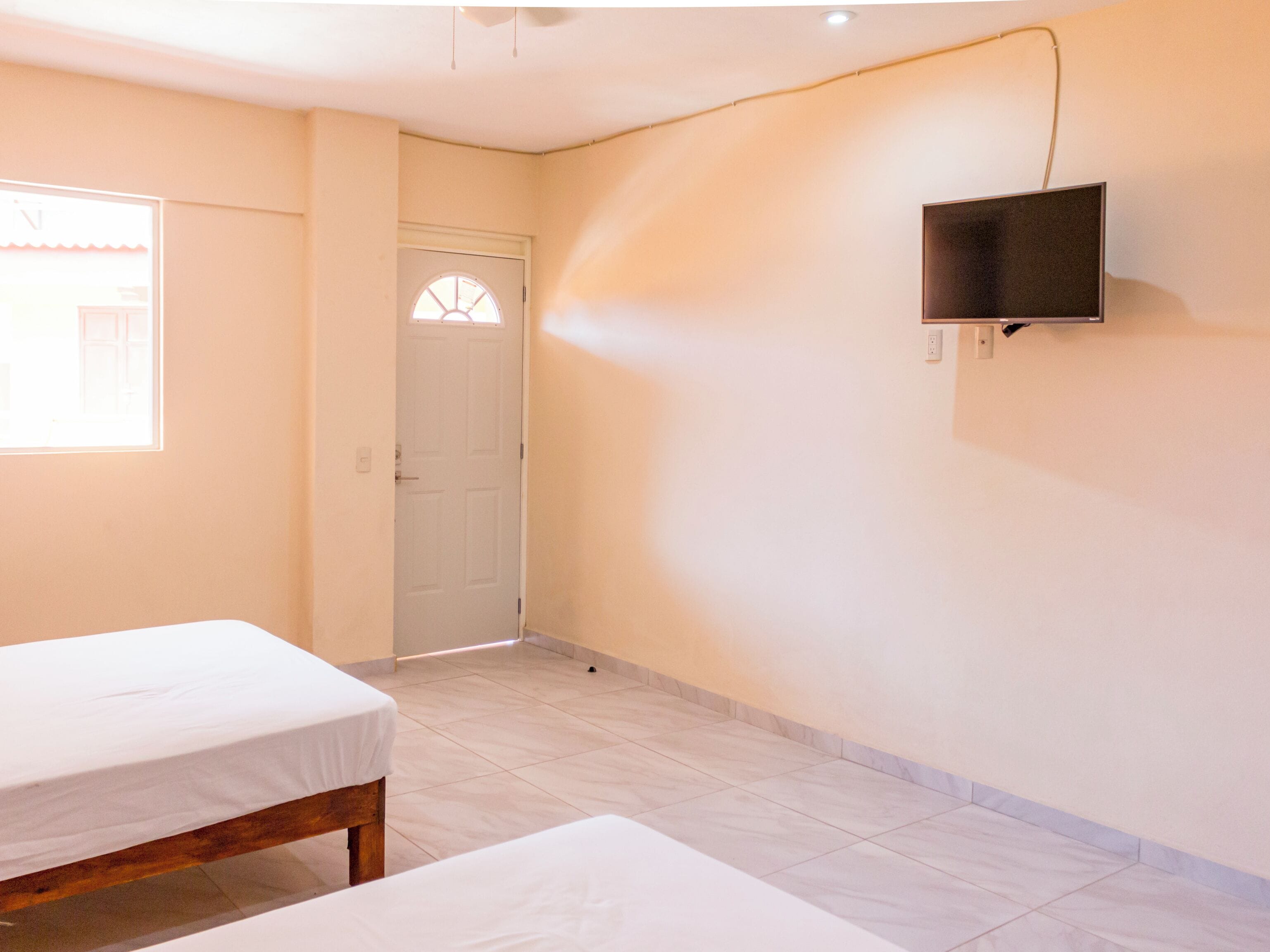 A room with two beds, a TV mounted on the wall, a door, and a window.