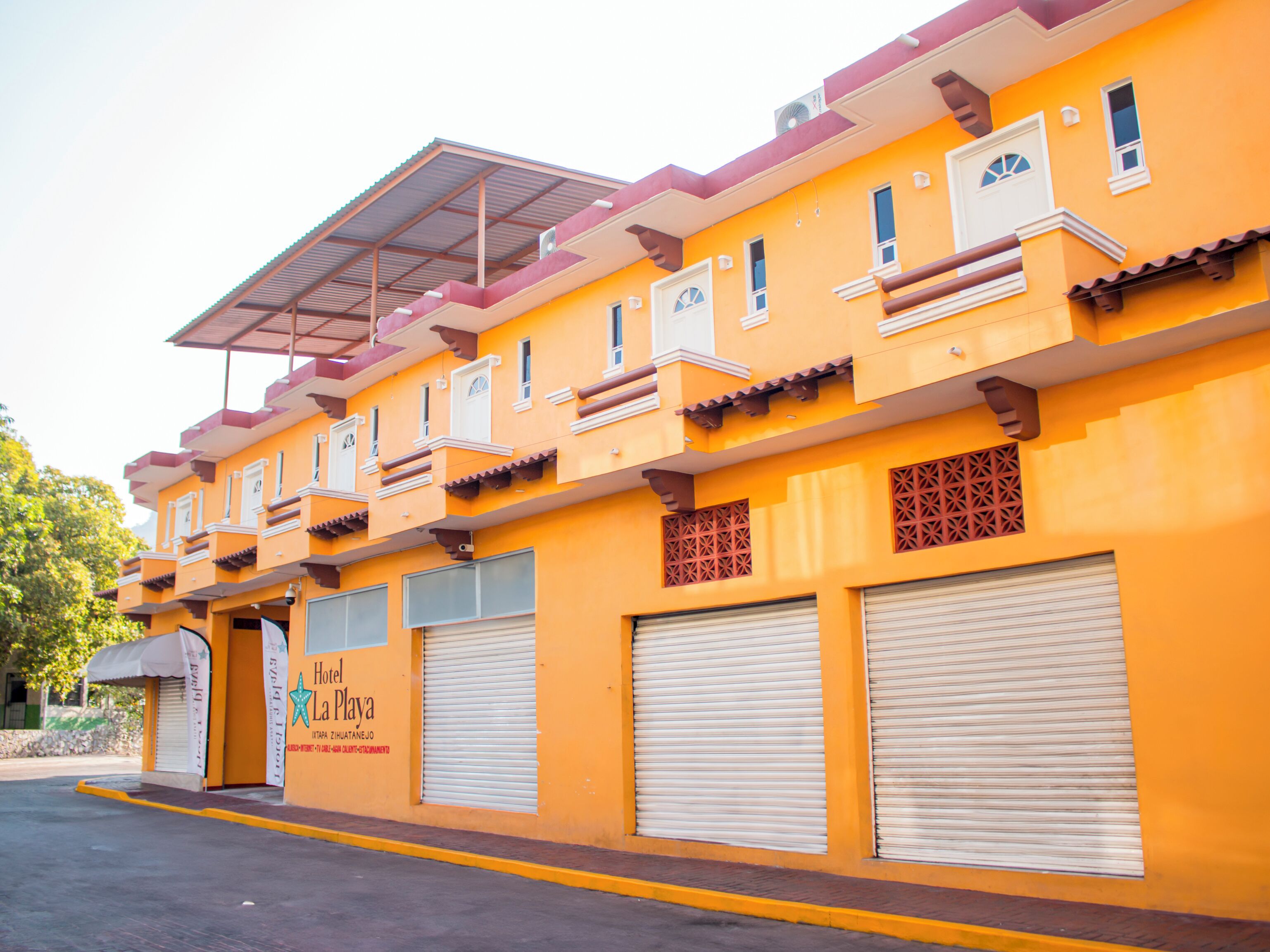 A hotel with a bright yellow facade, multiple balconies, and closed shutters.