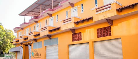 Un hotel con fachada amarilla brillante, varios balcones y persianas cerradas.