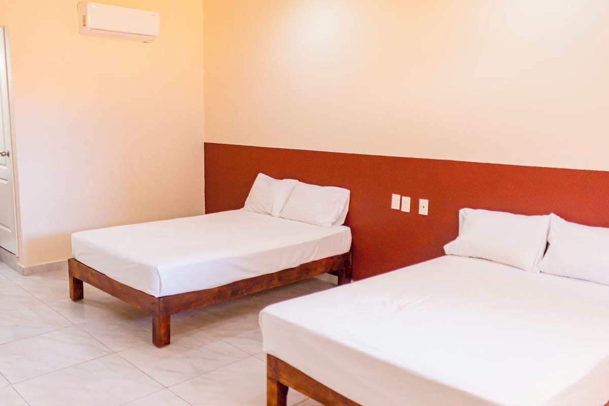Two single beds with wooden frames and white bedding in a room with white walls and a red accent wall.