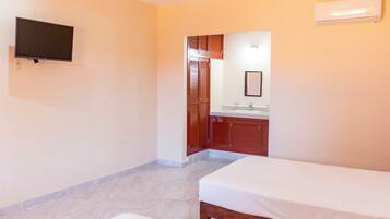 A hotel room with two single beds, a TV mounted on the wall, a bathroom with wooden cabinets, and a tiled floor.