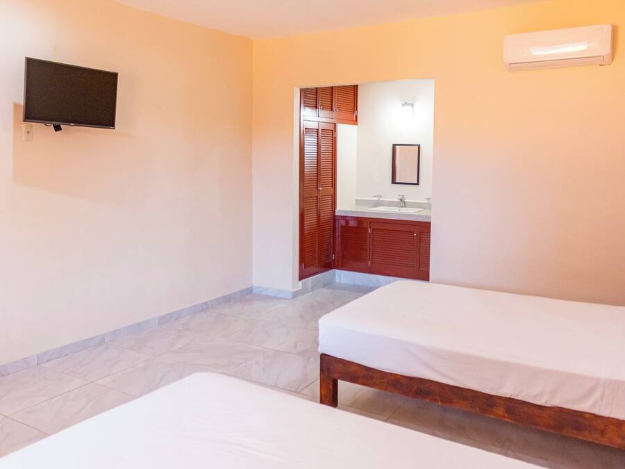 A hotel room with two single beds, a TV mounted on the wall, a bathroom with wooden cabinets, and a tiled floor.
