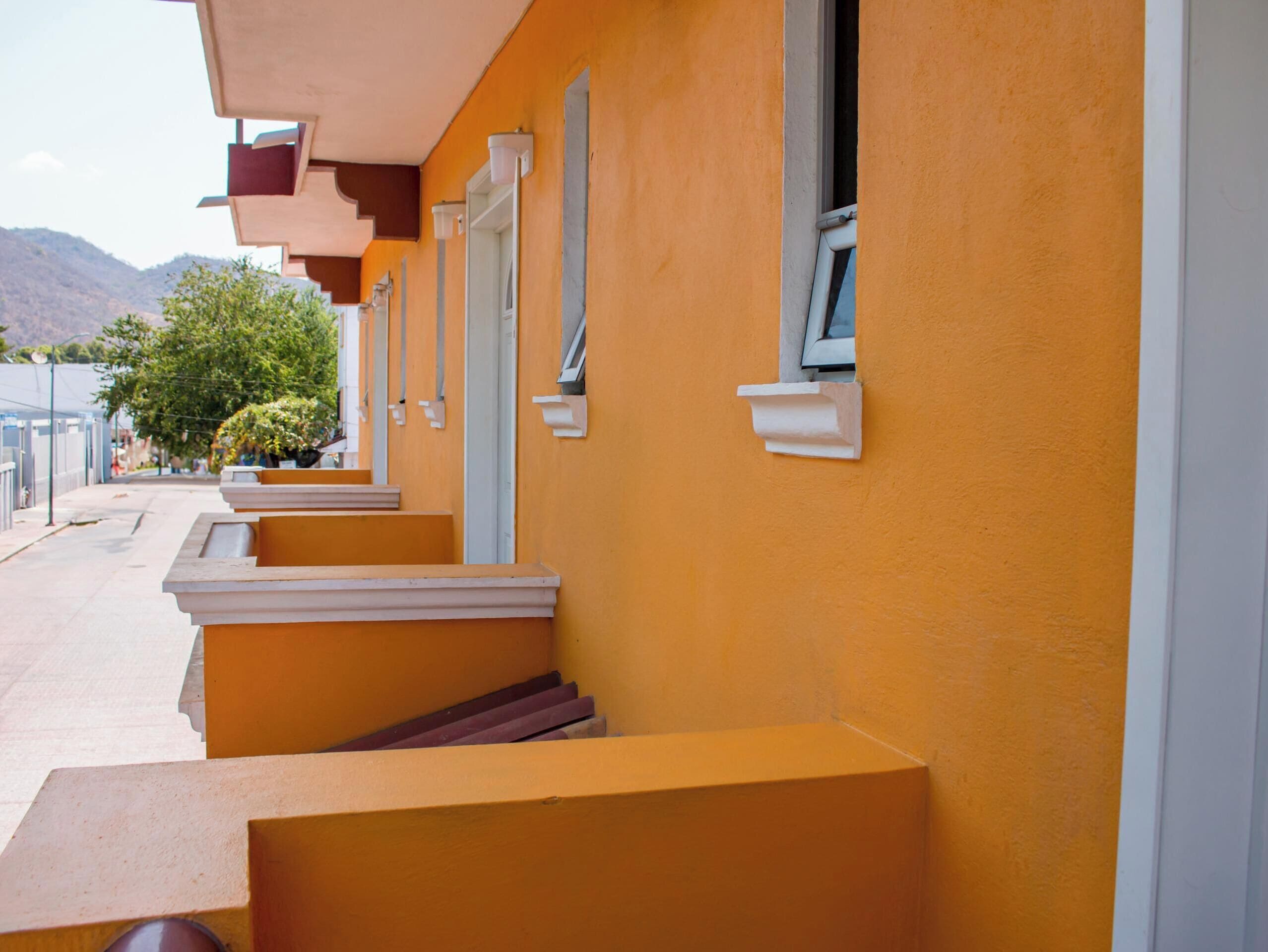 Una hilera de habitaciones de hotel con paredes anaranjadas y detalles blancos, con balcones y vistas a las montañas.