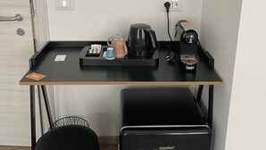 A compact room with a desk, a coffee maker, a kettle, a trash bin, and a suitcase. - The Platform Rooms (Ferrara)
