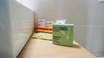Ein Badezimmer mit einer grünen Kiste mit dem Aufdruck 'ECO3ND: SOLIDO' und einer gelben Packung auf einem Holzregal.