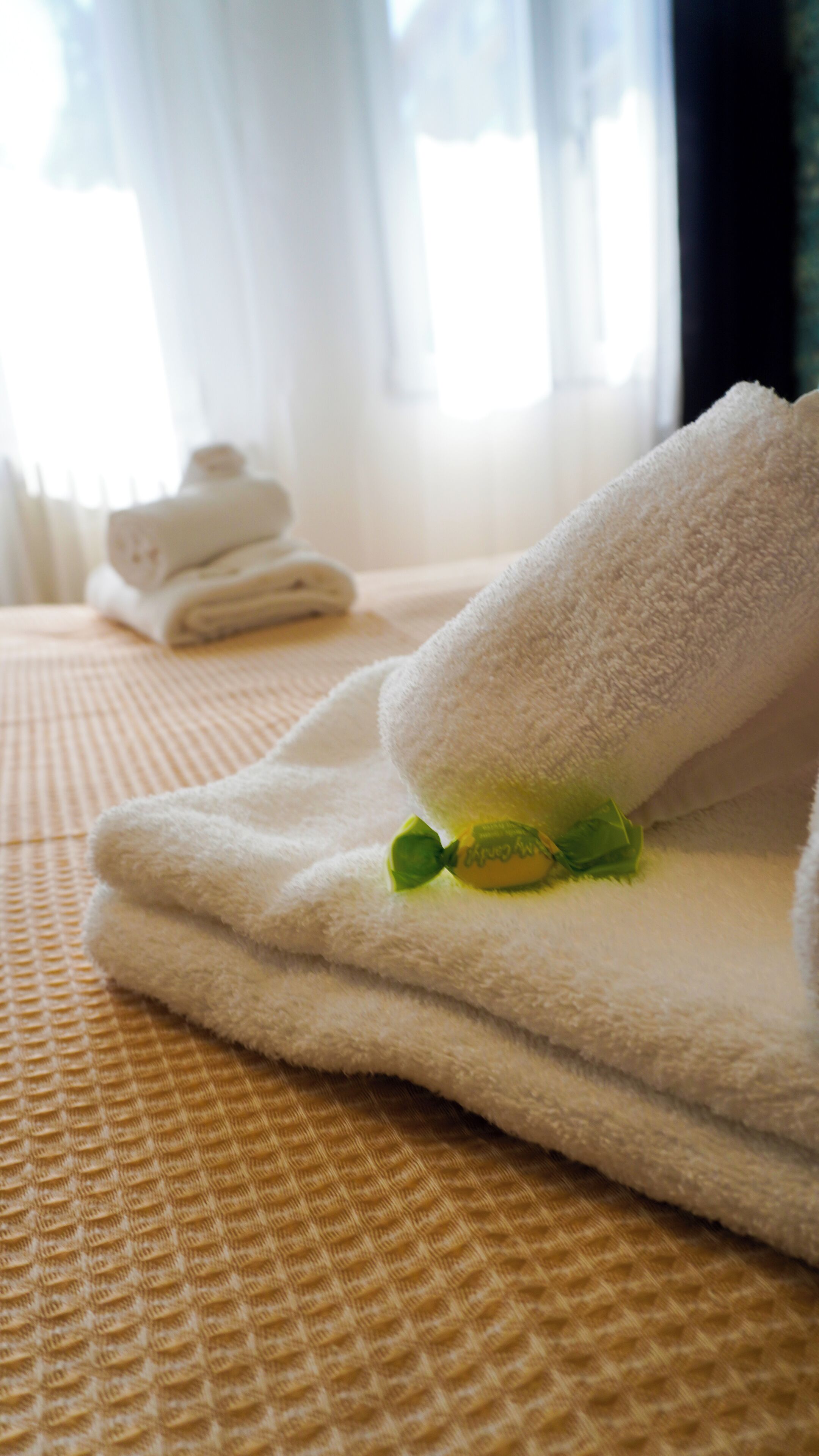 A neatly folded white towel with a green leaf, placed on a textured yellow bedspread.