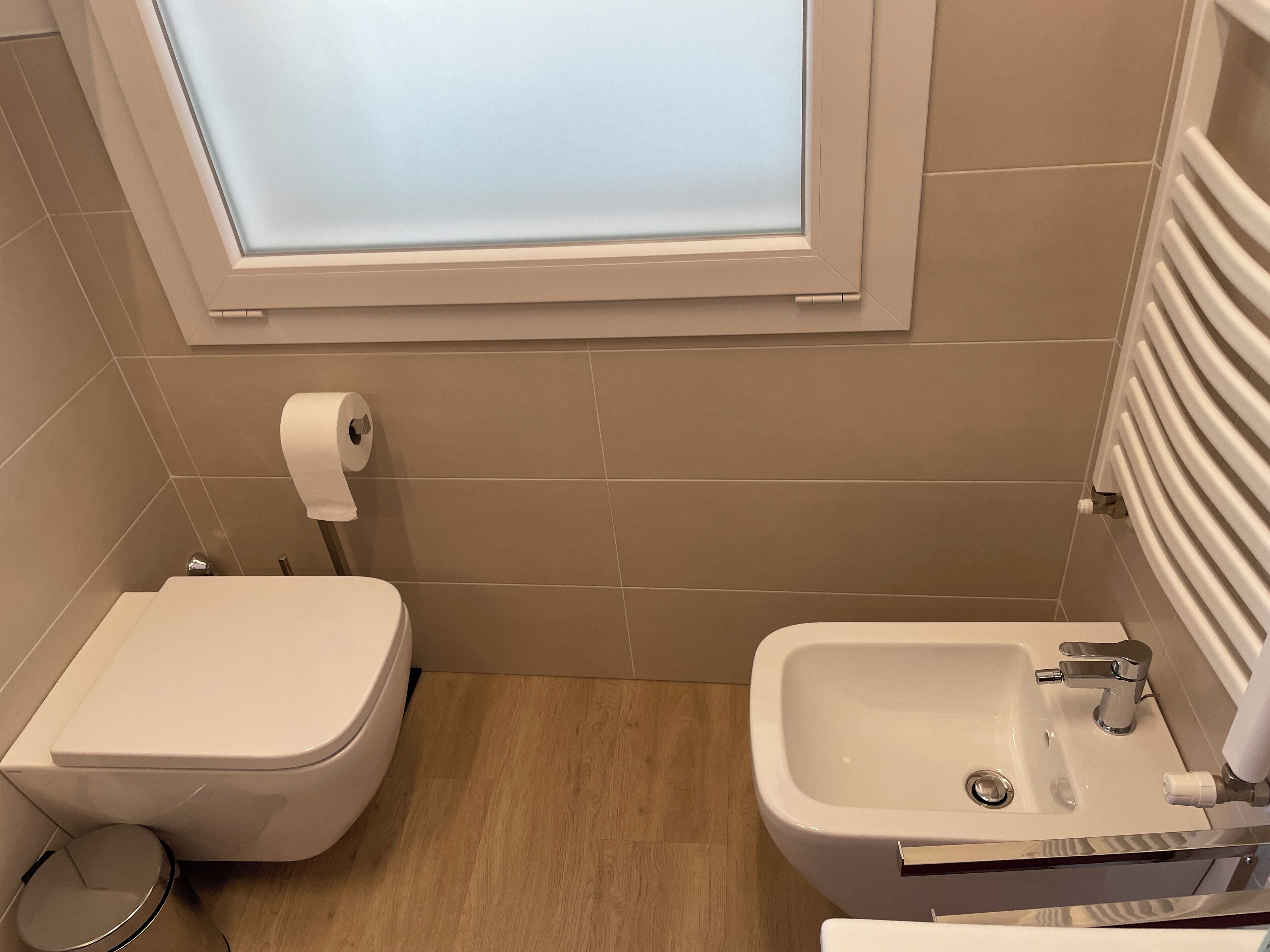 Un bagno piccolo con un water, un bidet e una finestra sopra il water.