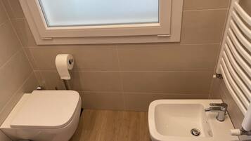 Un bagno piccolo con un water, un bidet e una finestra sopra il water.