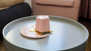A round table with a pink dessert on a plate, a chair, and a sofa in the background. - The Platform Rooms (Ferrara)