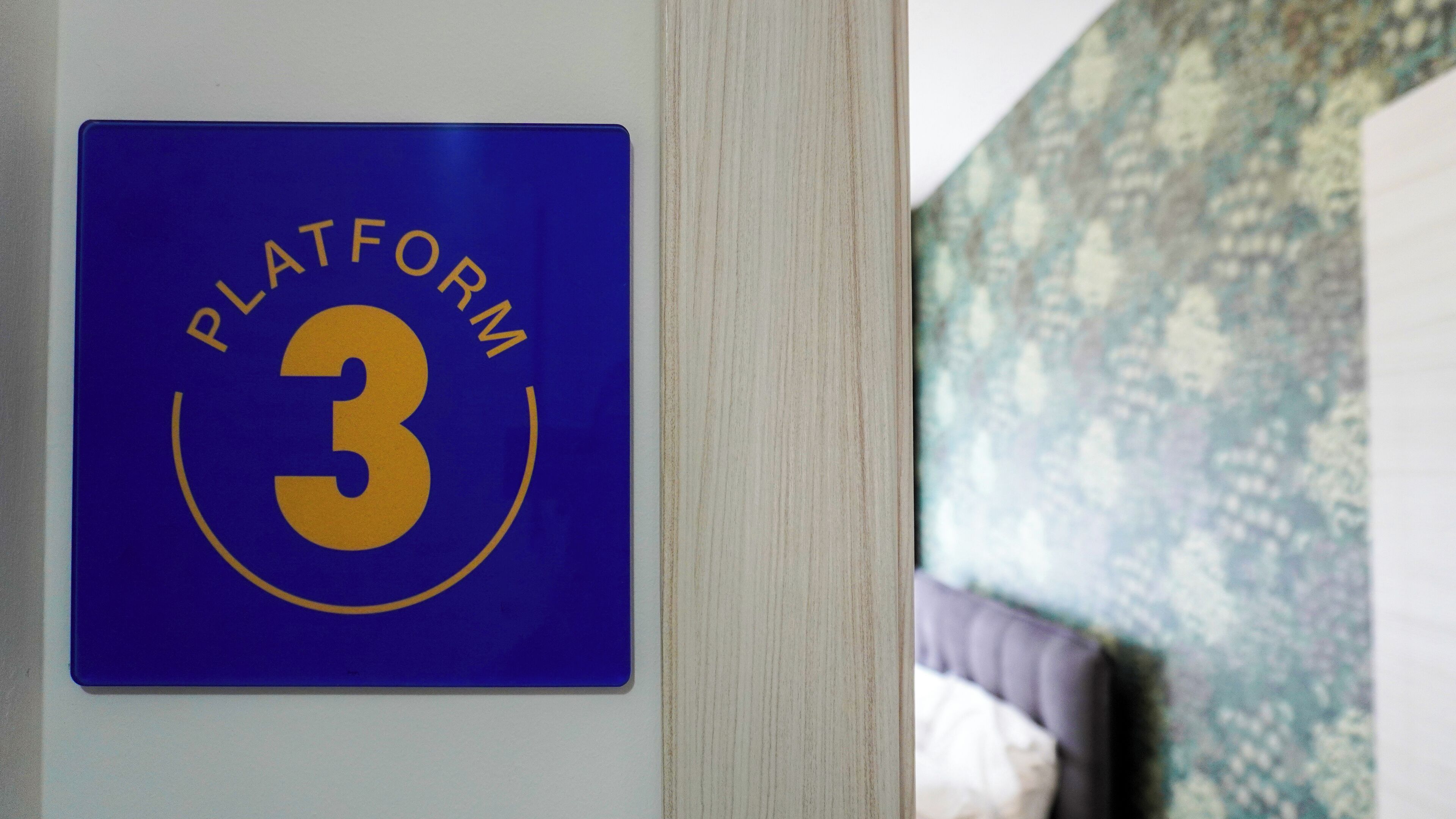Ein blaues Schild mit der Aufschrift 'PLATFORM 3' an einer Wand.