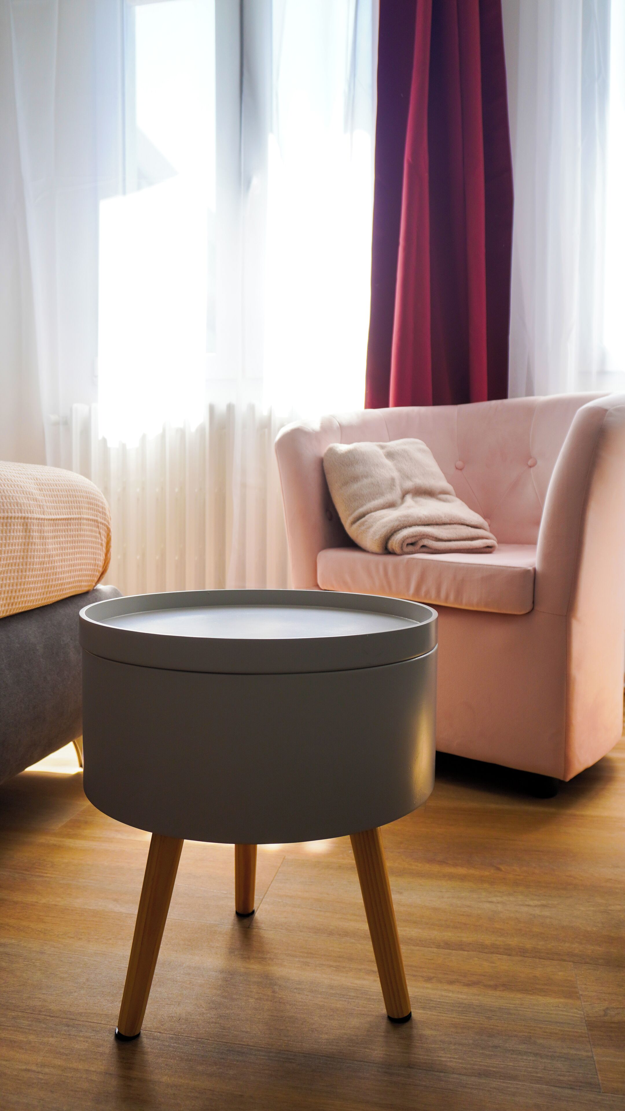 Un soggiorno moderno con un tavolo rotondo grigio, una poltrona rosa con una coperta beige e un pavimento in legno.